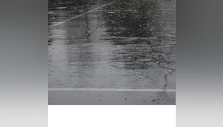 A wet, reflective pavement surface with visible raindrops and faint markings.
