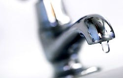 A close-up of a metal faucet with a droplet of water hanging from the spout.