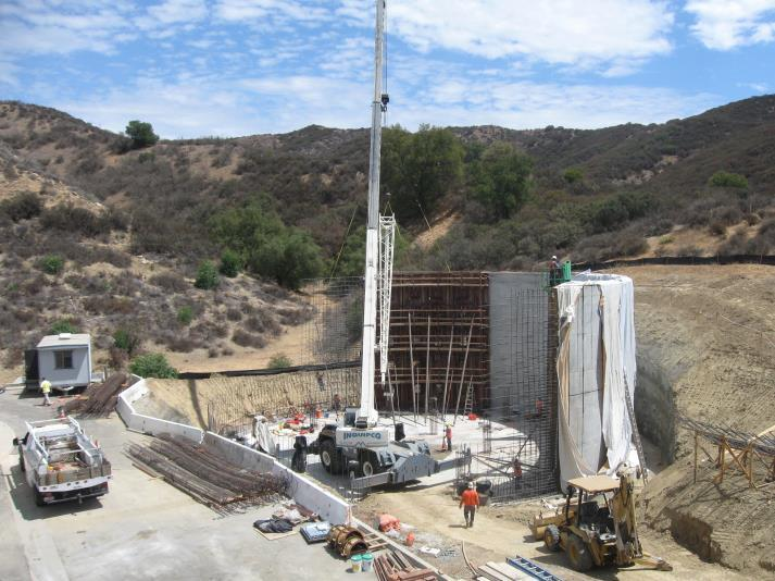 Construction site in a hilly area with a crane, vehicles, and workers.