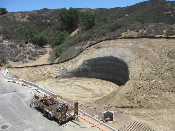 A large hole is dug into a hillside, with construction materials and a trailer nearby.