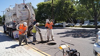Workers in safety gear using equipment to clean or repair a street manhole.