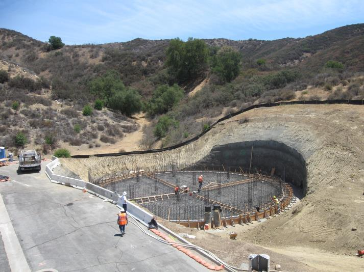 A construction site with workers building a circular foundation in a hilly, dry landscape.