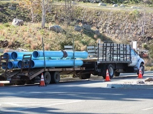 A truck carrying large blue pipes parked on the roadside, marked with orange cones.