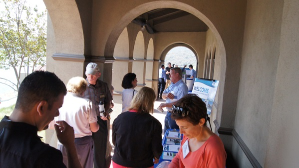 People networking at an outdoor event under an archway, with a "Welcome" sign on display.