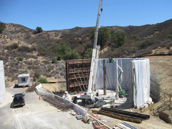 Construction site with a crane, workers, and a structure under development in a hilly, dry landscape.