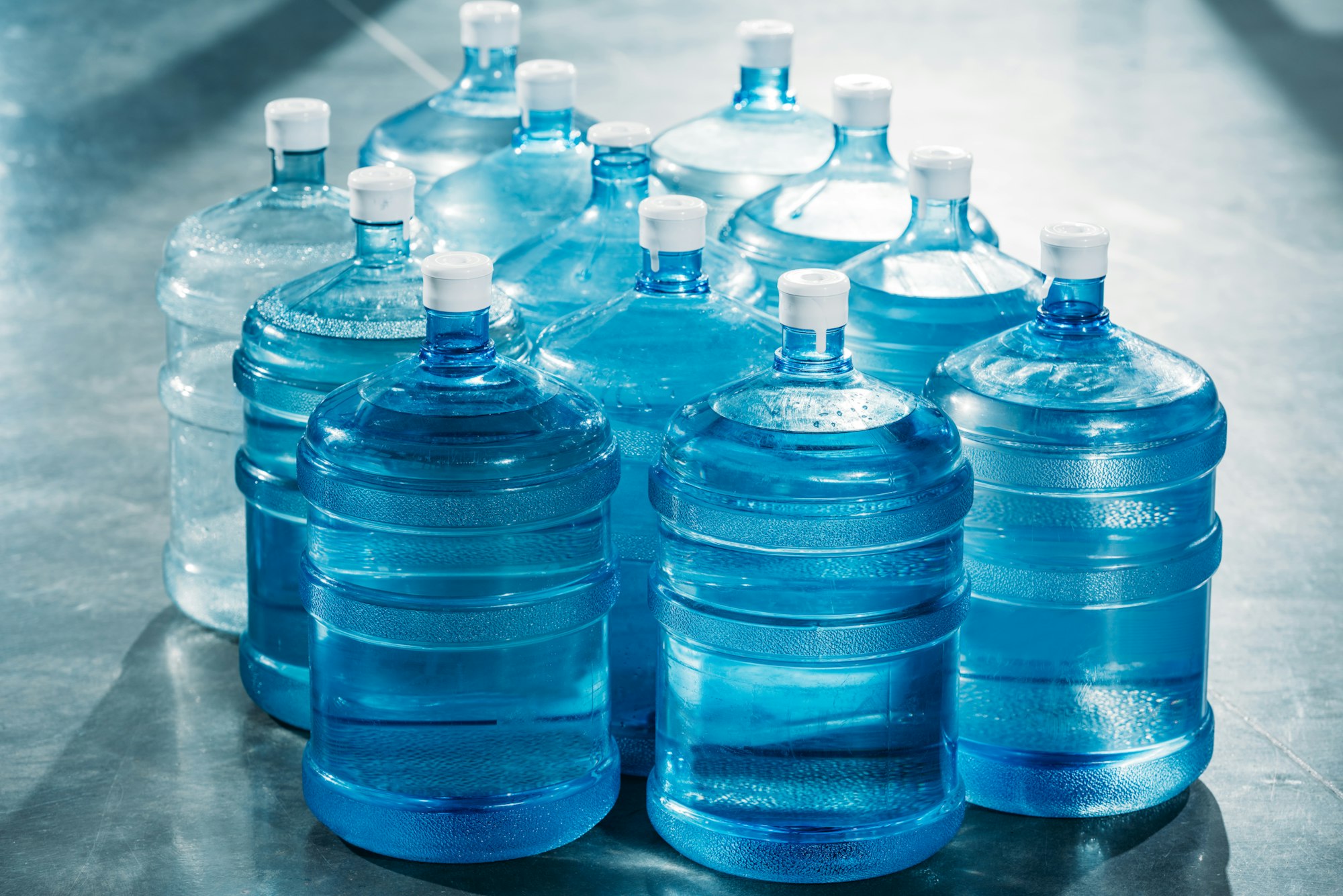 Large blue water containers with white caps on a shiny surface, illustrating having water for an emergency