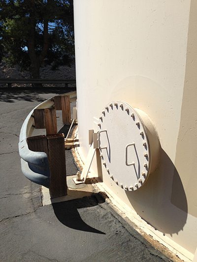 A large circular tank with a bolted access hatch and protective metal and wood barriers.