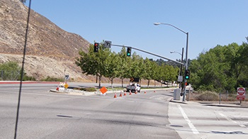 A road with traffic lights, orange cones, trees, and a truck at an intersection.