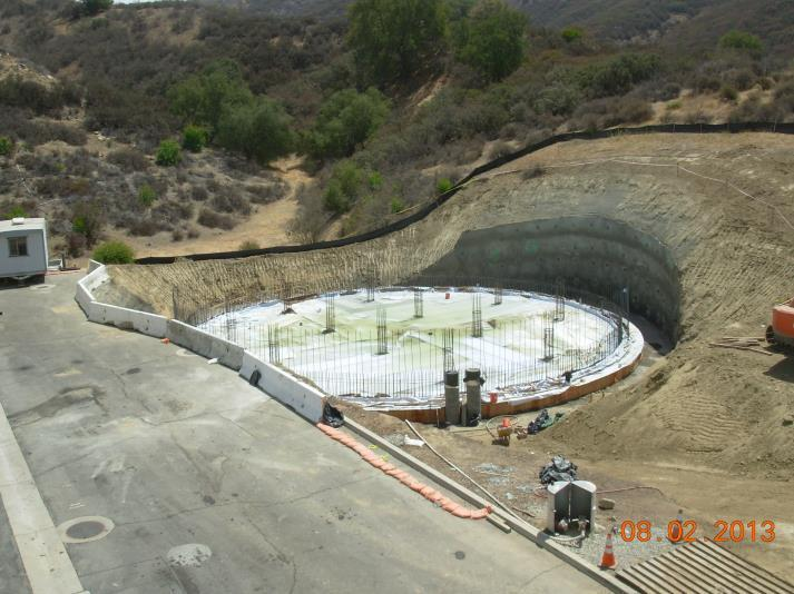 Construction site with a circular foundation in progress, surrounded by dirt and hills.
