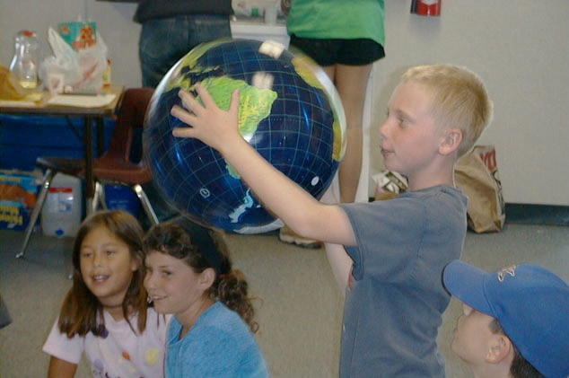 Children in a classroom, one holding a globe while others watch.