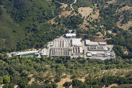 Aerial view of an industrial facility surrounded by forested hills and greenery.