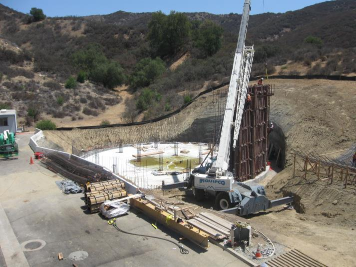 Construction site with a crane, workers, and building materials amid a hilly landscape.
