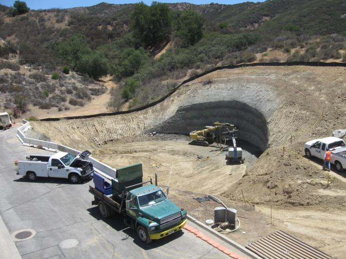 Construction site with trucks and machinery in a hilly area; soil excavation in progress.