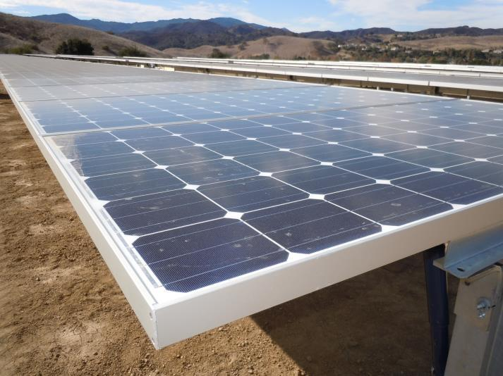 Solar panels installed on a sandy area with hills in the background.