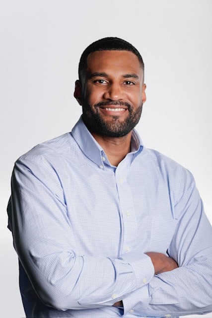 A person in a light blue shirt, smiling with arms crossed against a plain background.