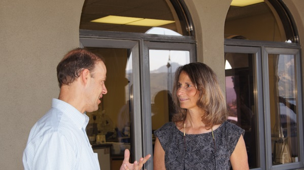 A man and a woman are having a conversation outside, near arched windows.