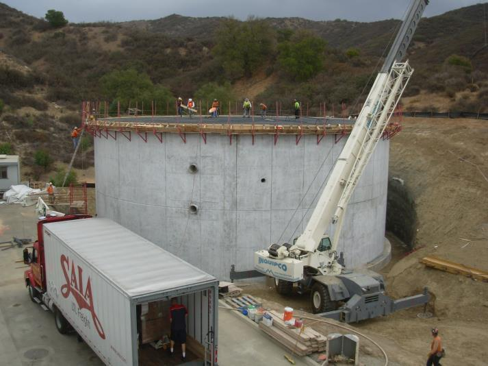 A construction site with a large round concrete structure, workers, a crane, and a truck with a "SALA" logo.