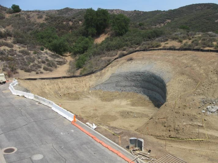 Construction site with a large dug-out area and erosion control measures, surrounded by hilly terrain with sparse vegetation.