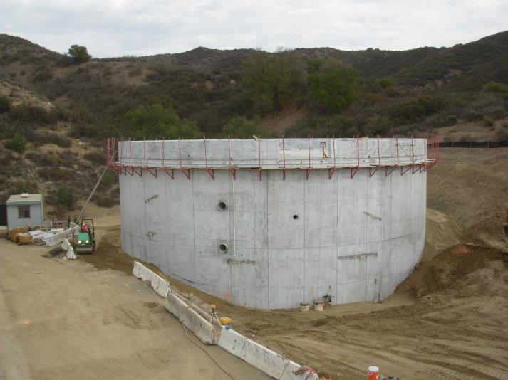 A large concrete cylindrical structure under construction with surrounding dirt and a small building nearby.