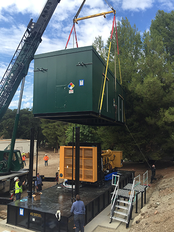 A crane is lifting a large green container onto a platform, with people guiding the process.
