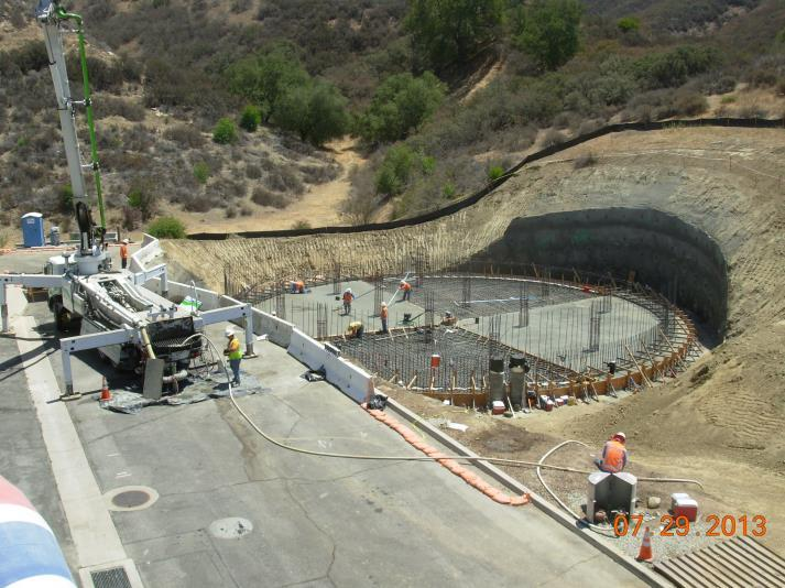 Construction site with workers, rebar, and machinery. Circular foundation formwork in a hilly area.