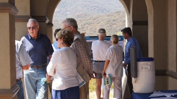 A group of people standing in an arched hallway, talking and looking at a display board, with a mountain landscape in the background.