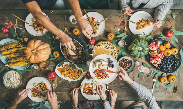 A festive table spread with various dishes, fruits, drinks, and a pumpkin, showcasing a communal meal experience.