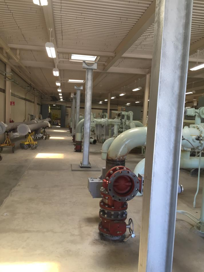 Industrial setting with pipes, machinery, and support beams in a large indoor facility.