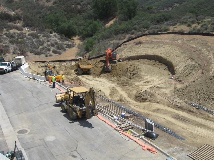 Construction site with heavy machinery, workers, and earthmoving in a hilly area.