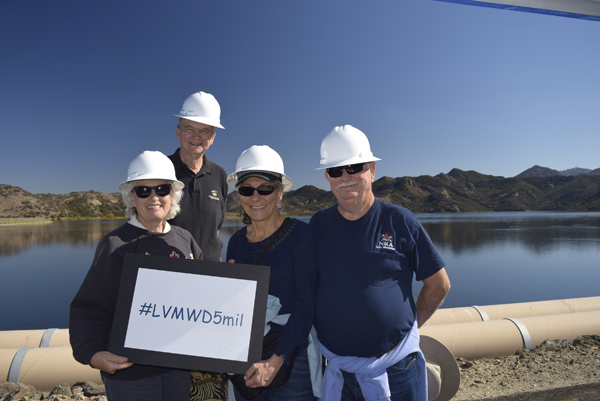 Four people in hard hats by a lake holding a sign reading "#LVMWD5mil."
