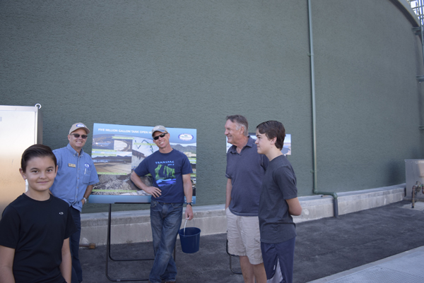 Five people standing outside near a poster about a tank in casual attire.