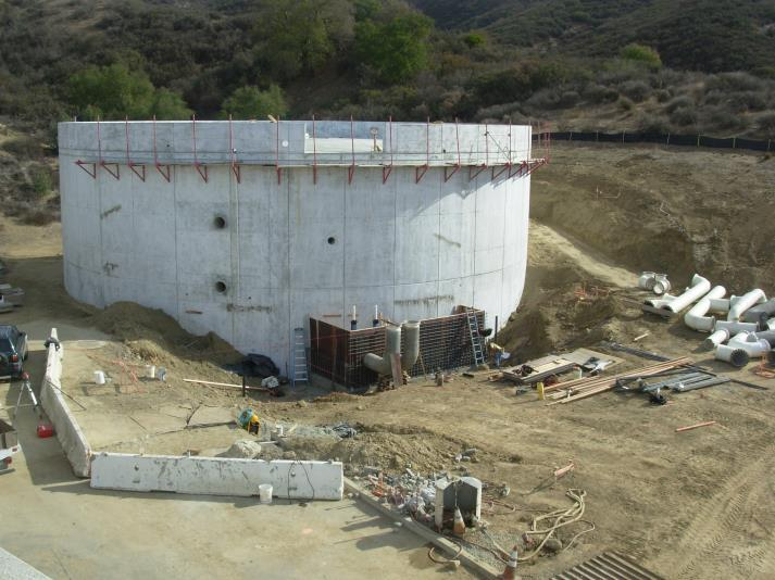 A large cylindrical concrete structure under construction with pipes and construction materials around it.