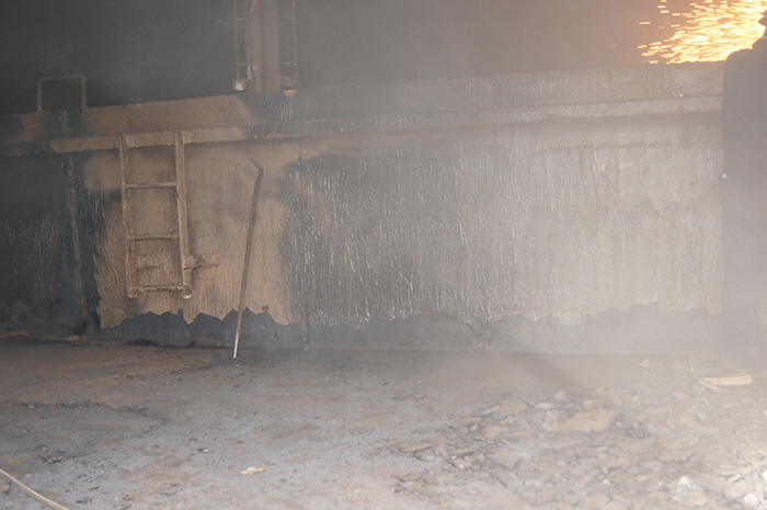 A smoky industrial scene with a metal wall, scattered debris, and sparks flying from the upper right corner.