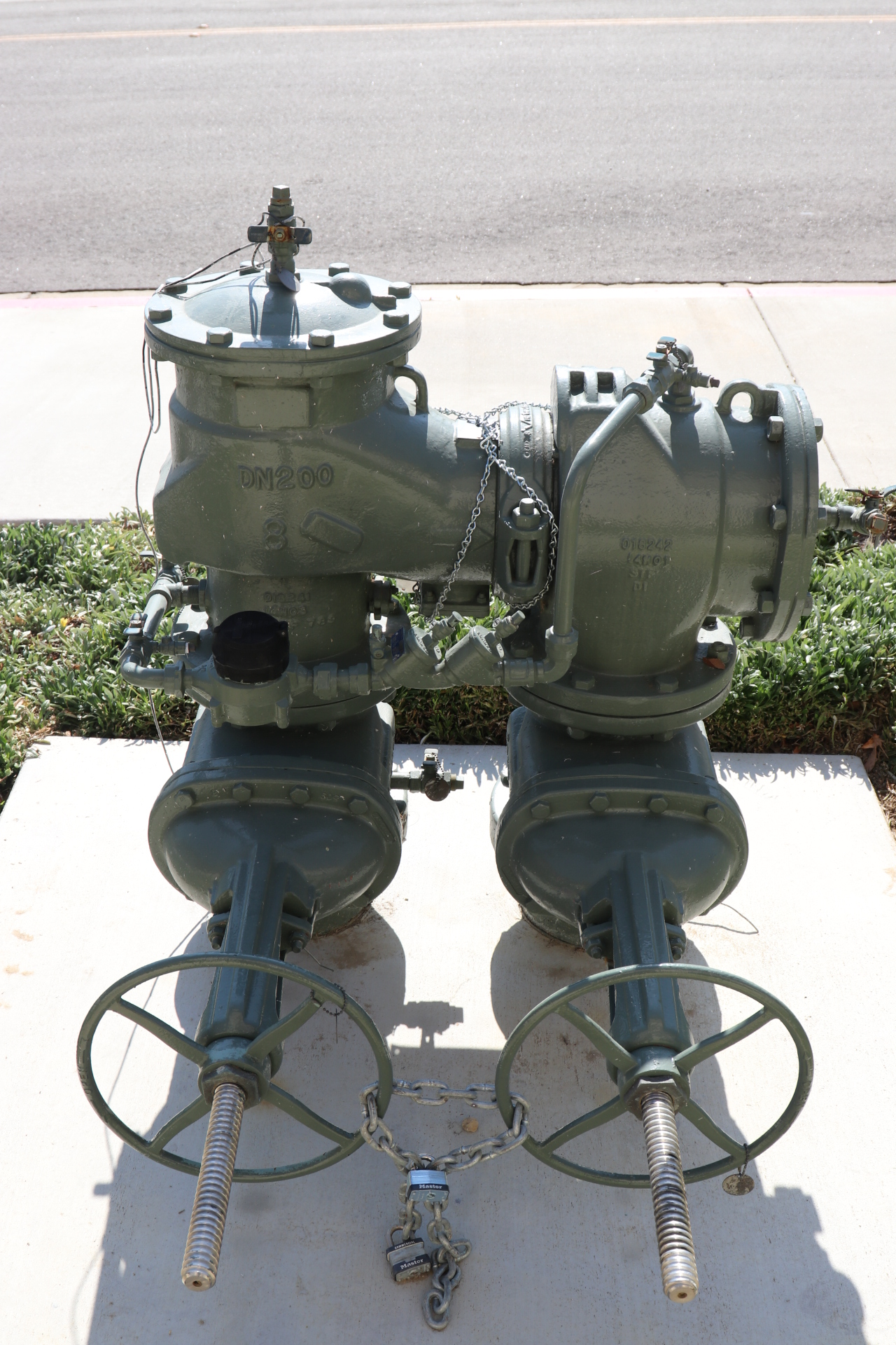 Two large industrial valves with wheels, joined by a chain and lock, placed on a concrete platform.