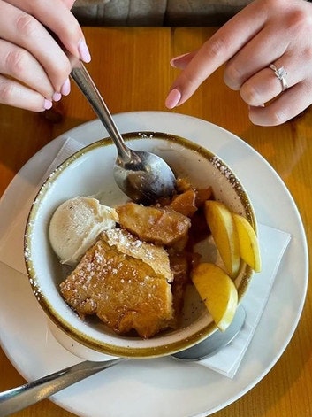 A dish with a slice of pie, vanilla ice cream, and lemon wedges, with hands holding a spoon.