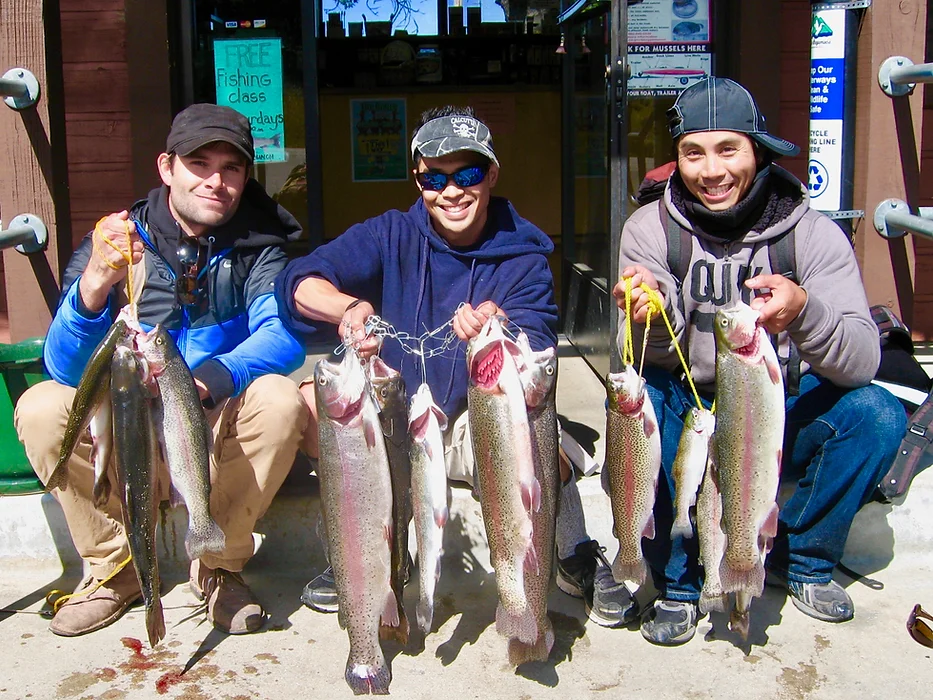 Three people posing with large fish outside a shop.