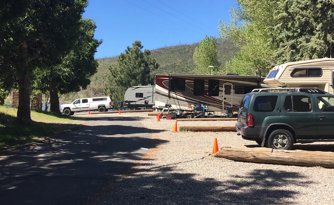 RVs and cars parked at a campsite surrounded by trees and mountains, with orange cones marking parking areas.