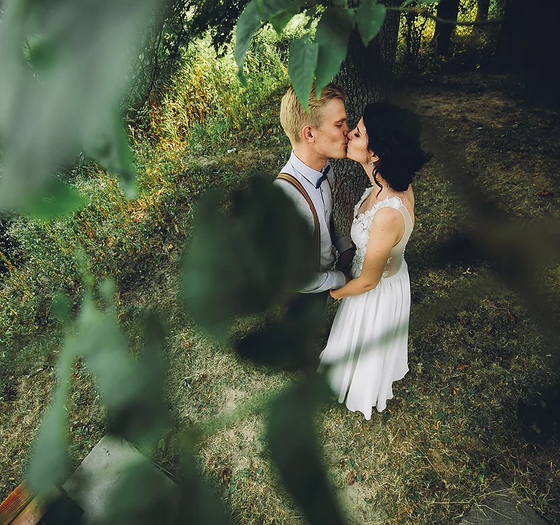 A couple kissing outdoors, framed through leaves, with a romantic atmosphere.
