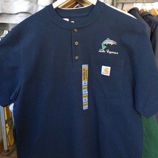 A navy blue polo shirt with "Lake Cayuga" embroidery and a fish design, featuring a Carhartt logo on the pocket, hanging on a rack.