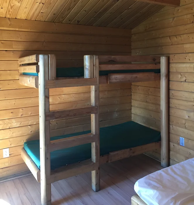 Wooden bunk beds with green mattresses in a cabin-like room.