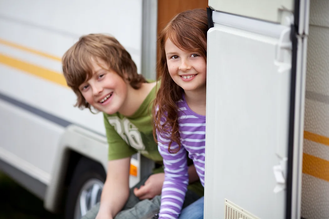 Two kids smiling, leaning out of a camper van.