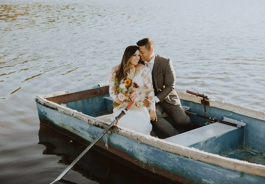 A couple in a boat on a lake, the woman holding flowers.