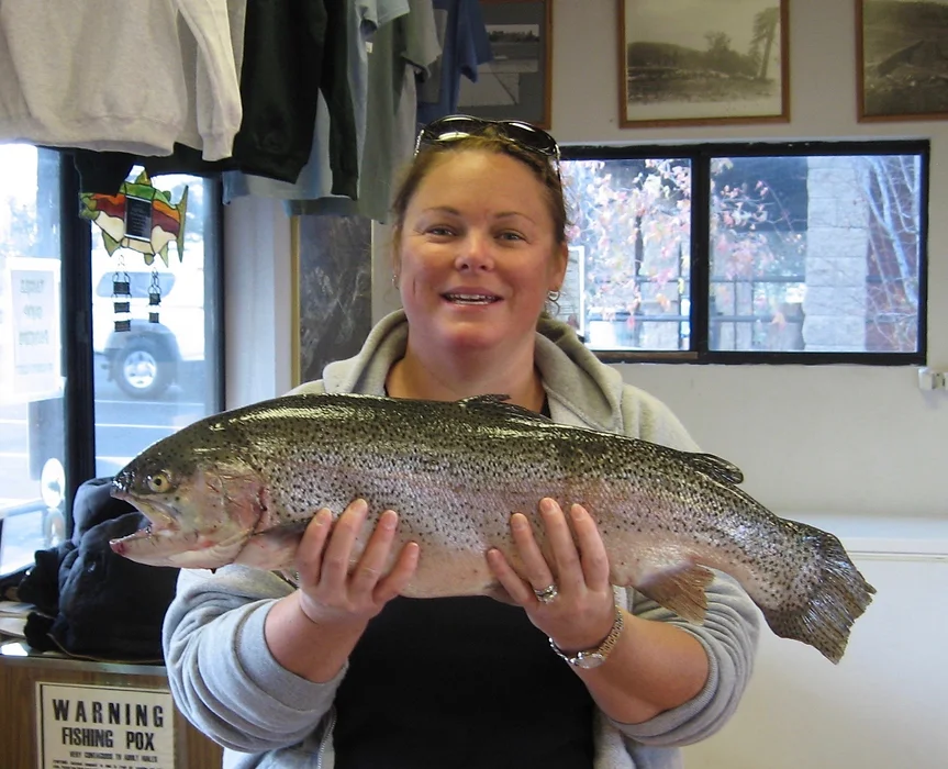 A person holding a large fish indoors, with clothes hanging and framed pictures in the background.