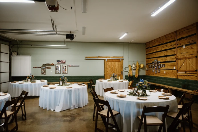 Room set for an event with round tables, white tablecloths, wooden chairs, and wall decorations.