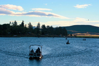 People in boats on a lake, surrounded by trees and hills under a partly cloudy sky.