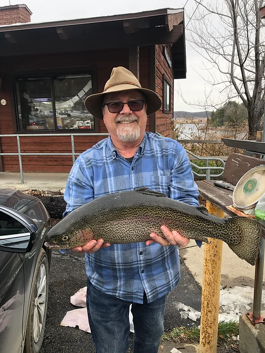 A person wearing a hat and glasses is holding a large fish outside a building.
