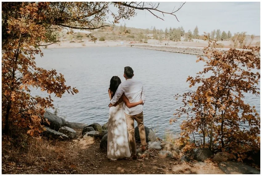 A couple embraces while overlooking a serene lake, surrounded by autumn foliage.