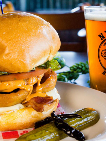 Burger with onion rings and bacon, pickles on the side, and a glass of beer.
