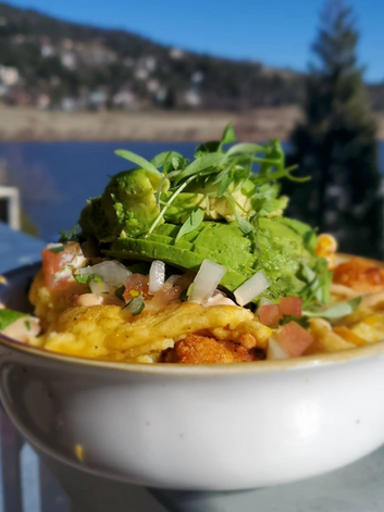 A bowl of food with avocado, greens, tomatoes, and omelette, set against a scenic outdoor background.