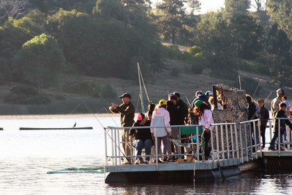 A group of people on a floating platform near a lake, surrounded by trees.